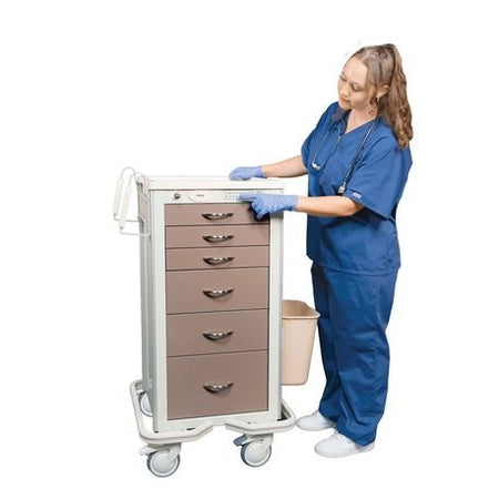 A healthcare professional in blue scrubs is interacting with a narrow, aluminum medical cart with multiple drawers. The cart is equipped with a lock mechanism and the person is using a key override.