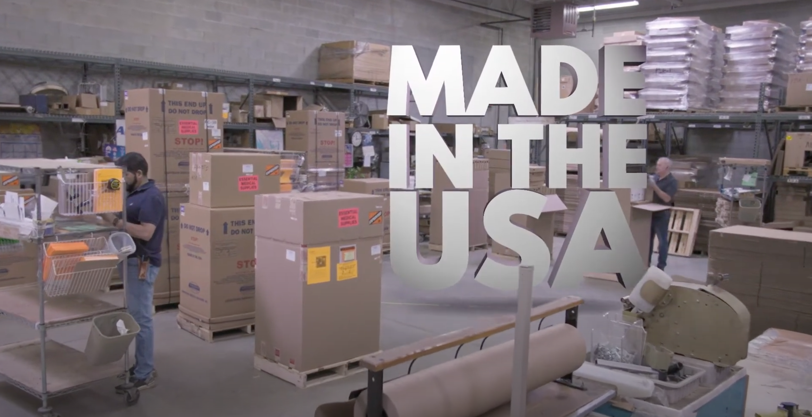 Load video: Interior of a busy warehouse with workers organizing stacks of boxes, overlaid with the text &#39;Made in the USA&#39;.